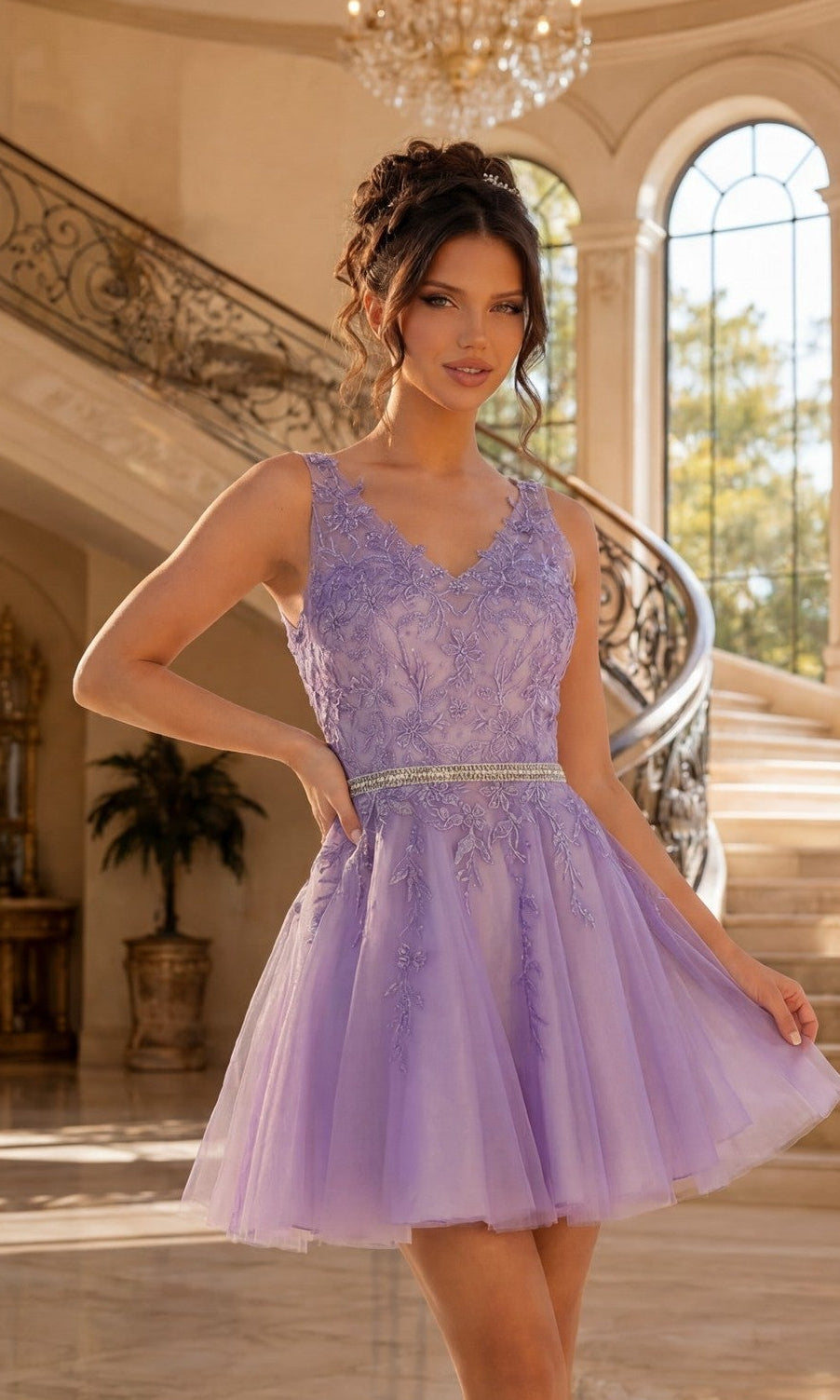 A woman stands indoors in front of a curved staircase and large windows, wearing a lilac Short Prom Dress with an embroidered sheer bodice and beaded waistband.